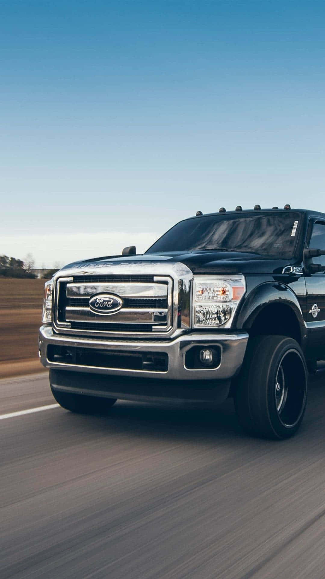 A Black Ford Super Duty Truck Is Driving Down The Road Wallpaper