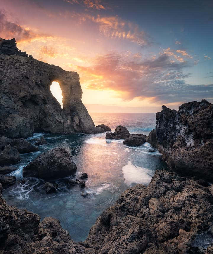 A Rock Arch At Sunset In The Ocean