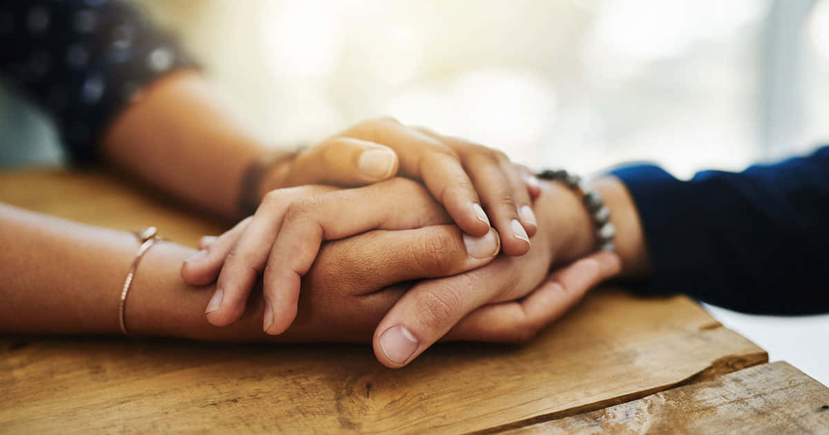 Two People Holding Hands On A Wooden Table