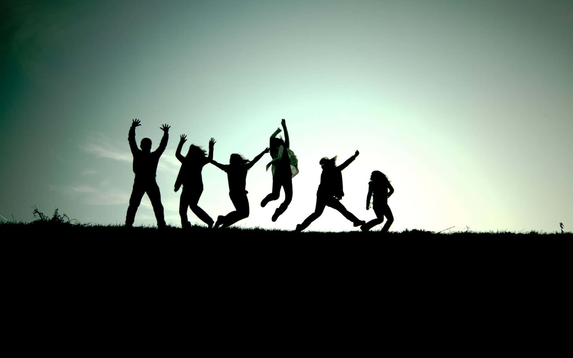 Silhouette Of People Jumping On A Hill