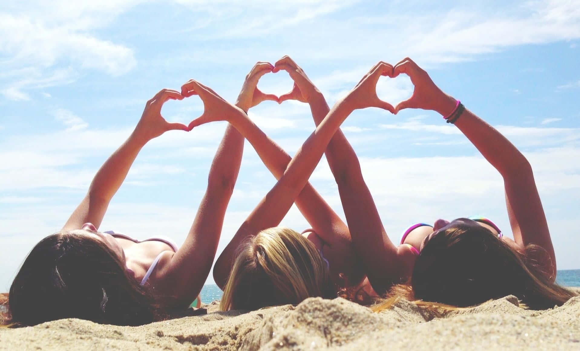 Tre kvinder laver et hjerteformet på stranden