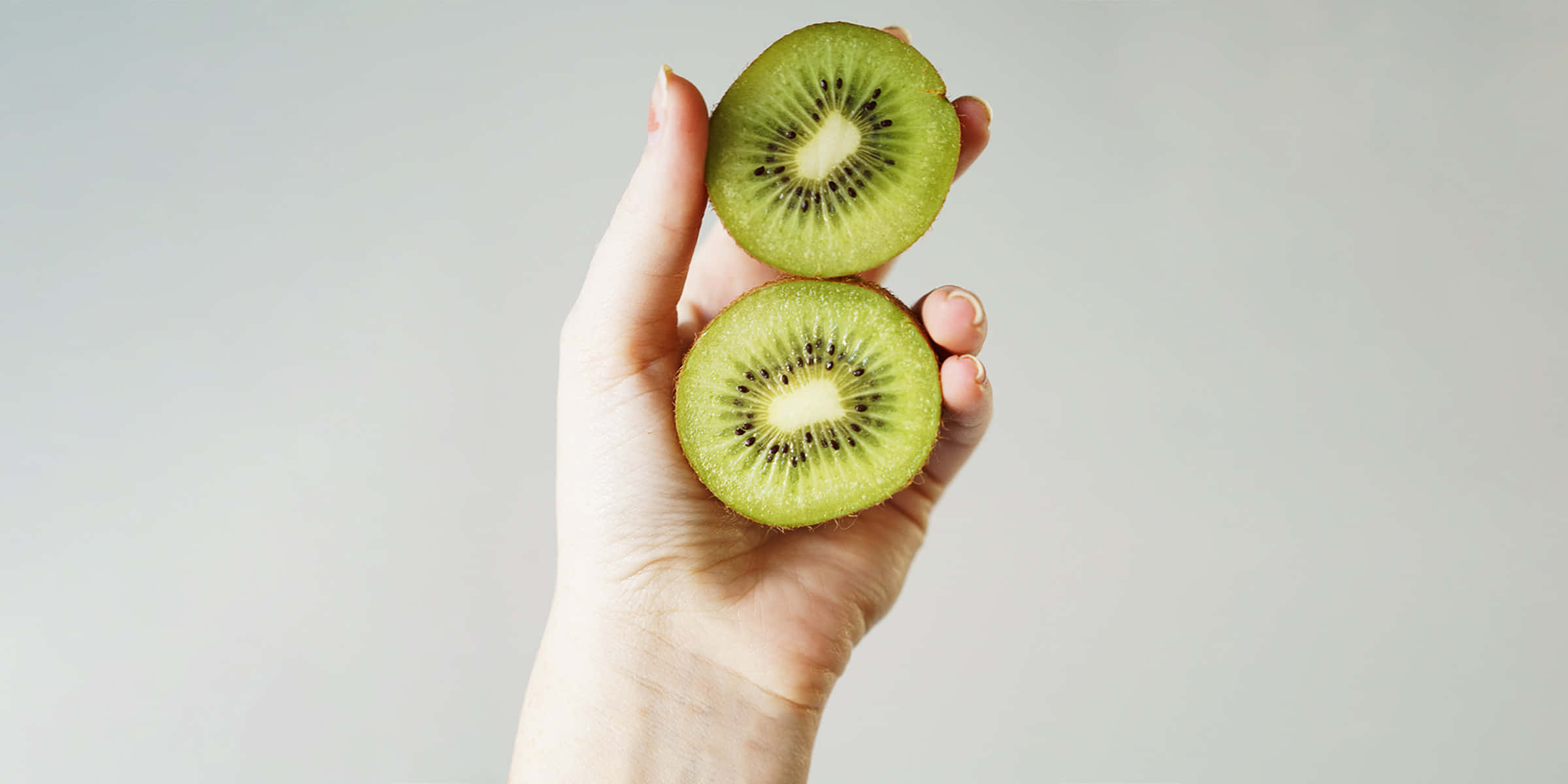 A Woman's Hand Holding Two Kiwi Slices