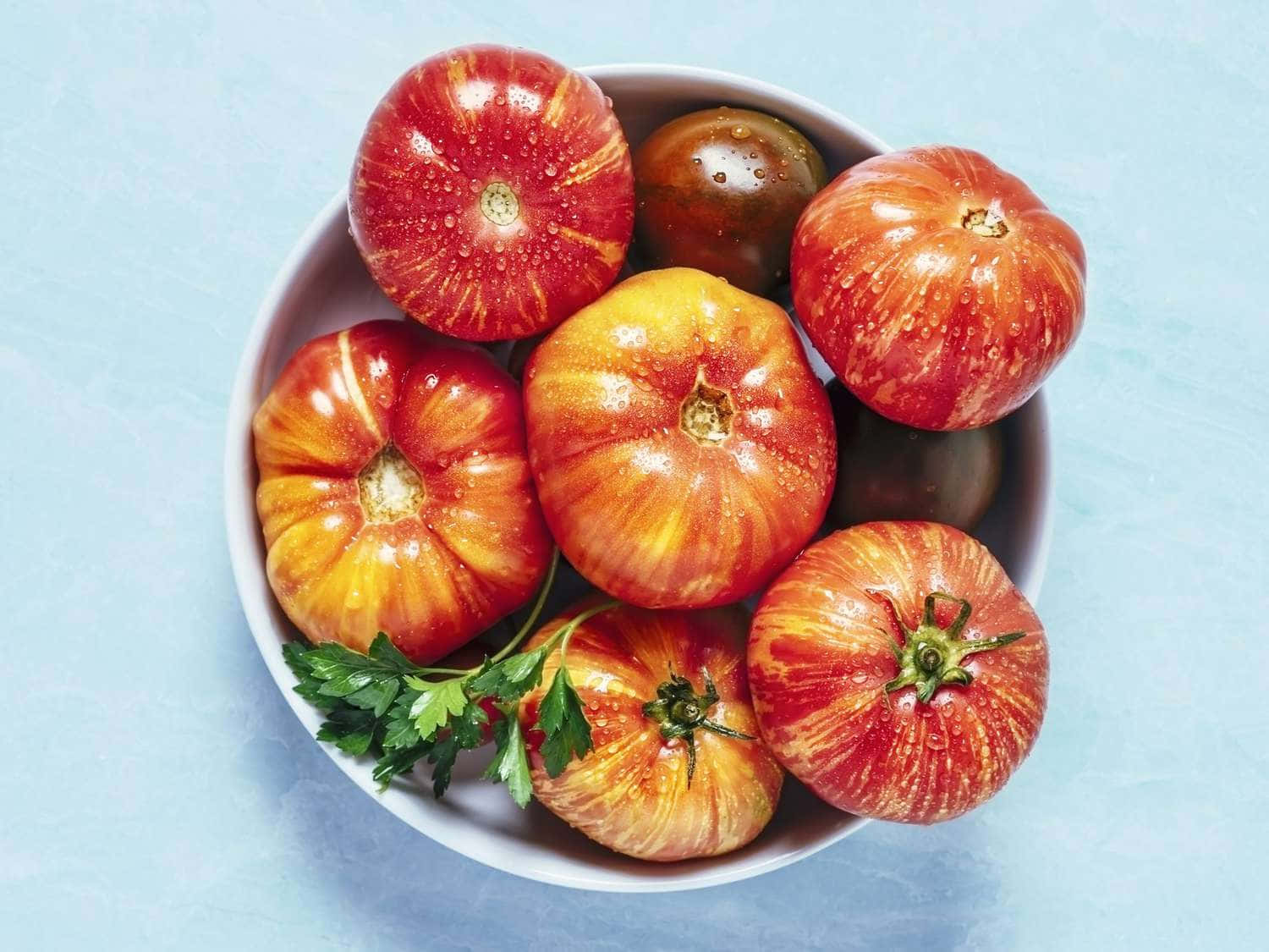A Bowl Of Tomatoes With Herbs On A Blue Surface