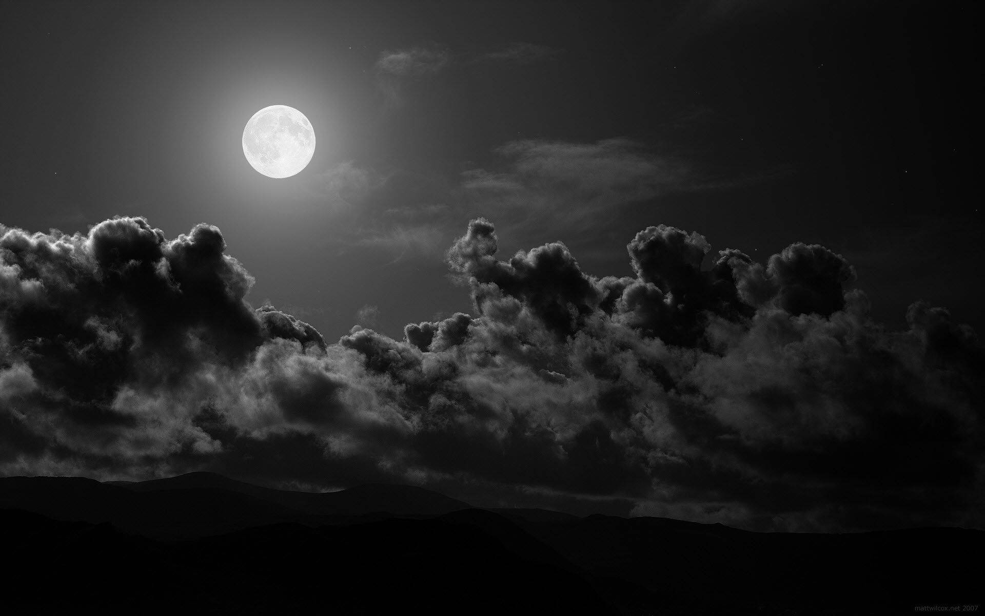 A view of a full moon shrouded in dark clouds on a black night Wallpaper