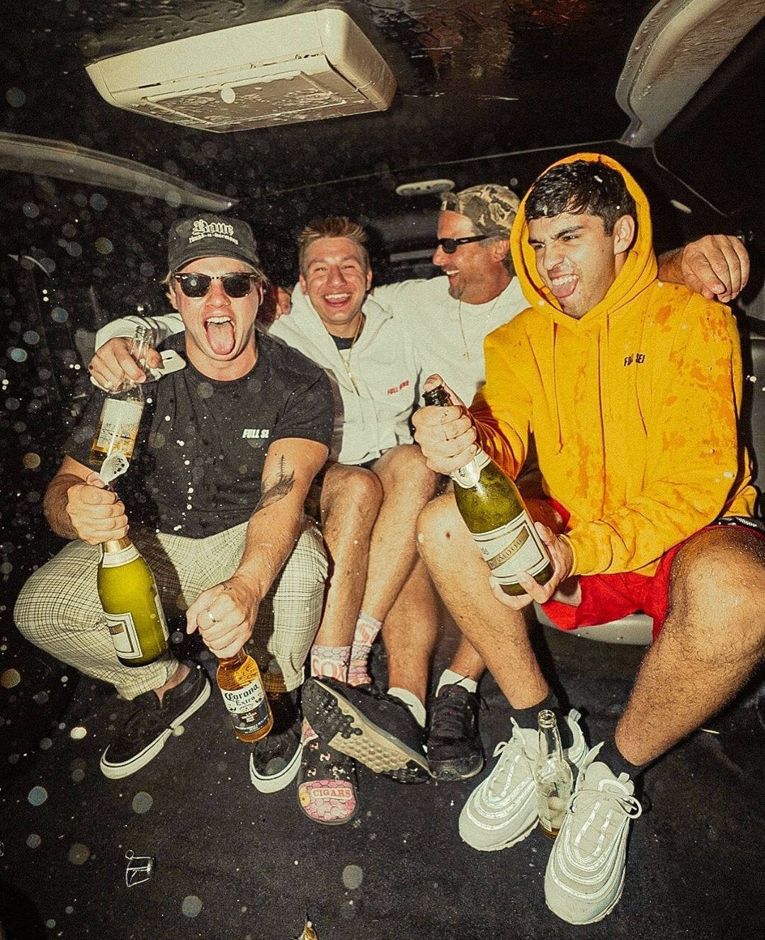 Fire mænd sidder i bagsædet af en bil med flasker af champagne. Wallpaper