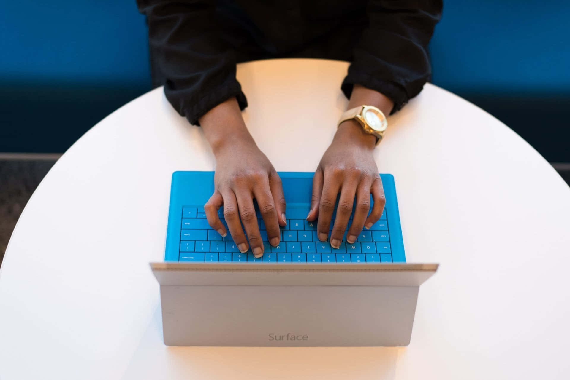 A Woman Is Typing On A Blue Surface Laptop