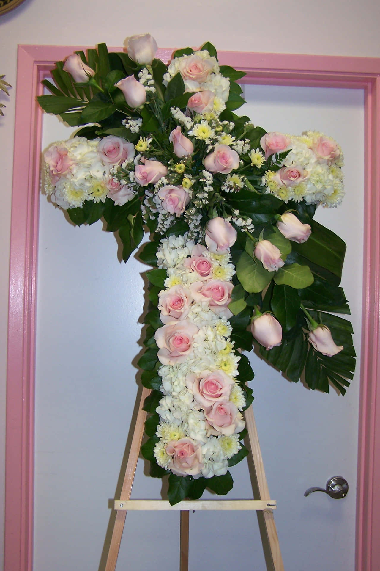 A Pink And White Cross With Flowers On A Pink Stand