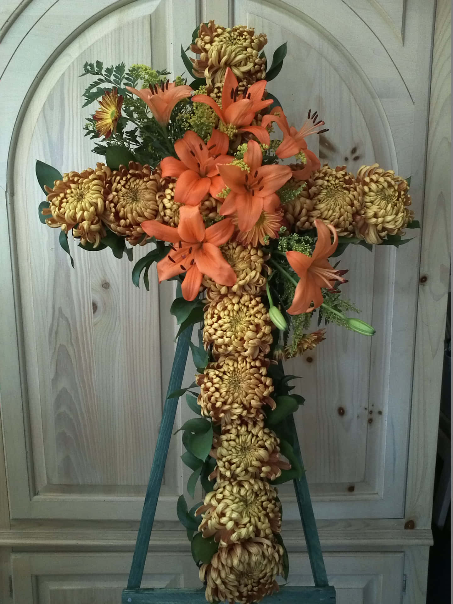 A Cross With Orange Flowers And Lilies On A Stand