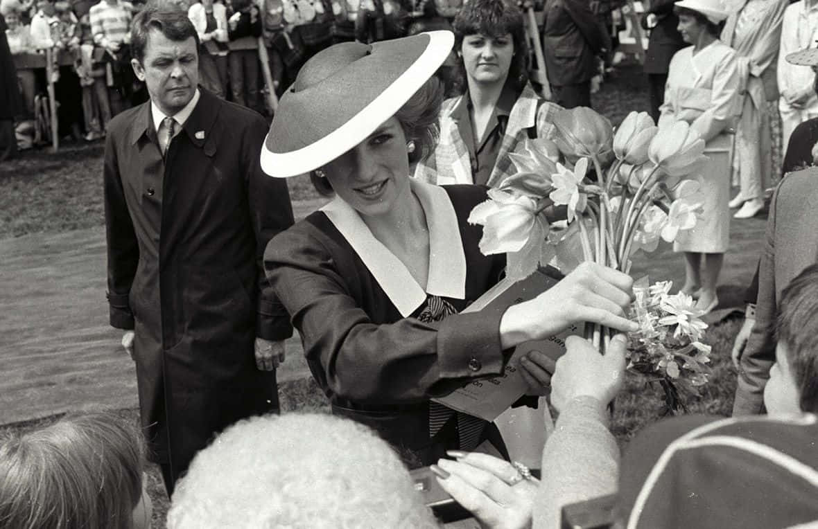 A Woman In A Hat Is Handing Flowers To People