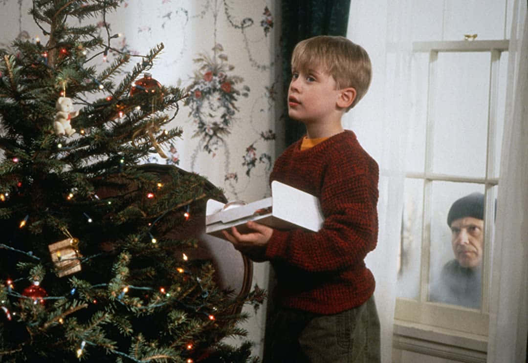 En dreng står ved siden af ​​et juletræ Wallpaper