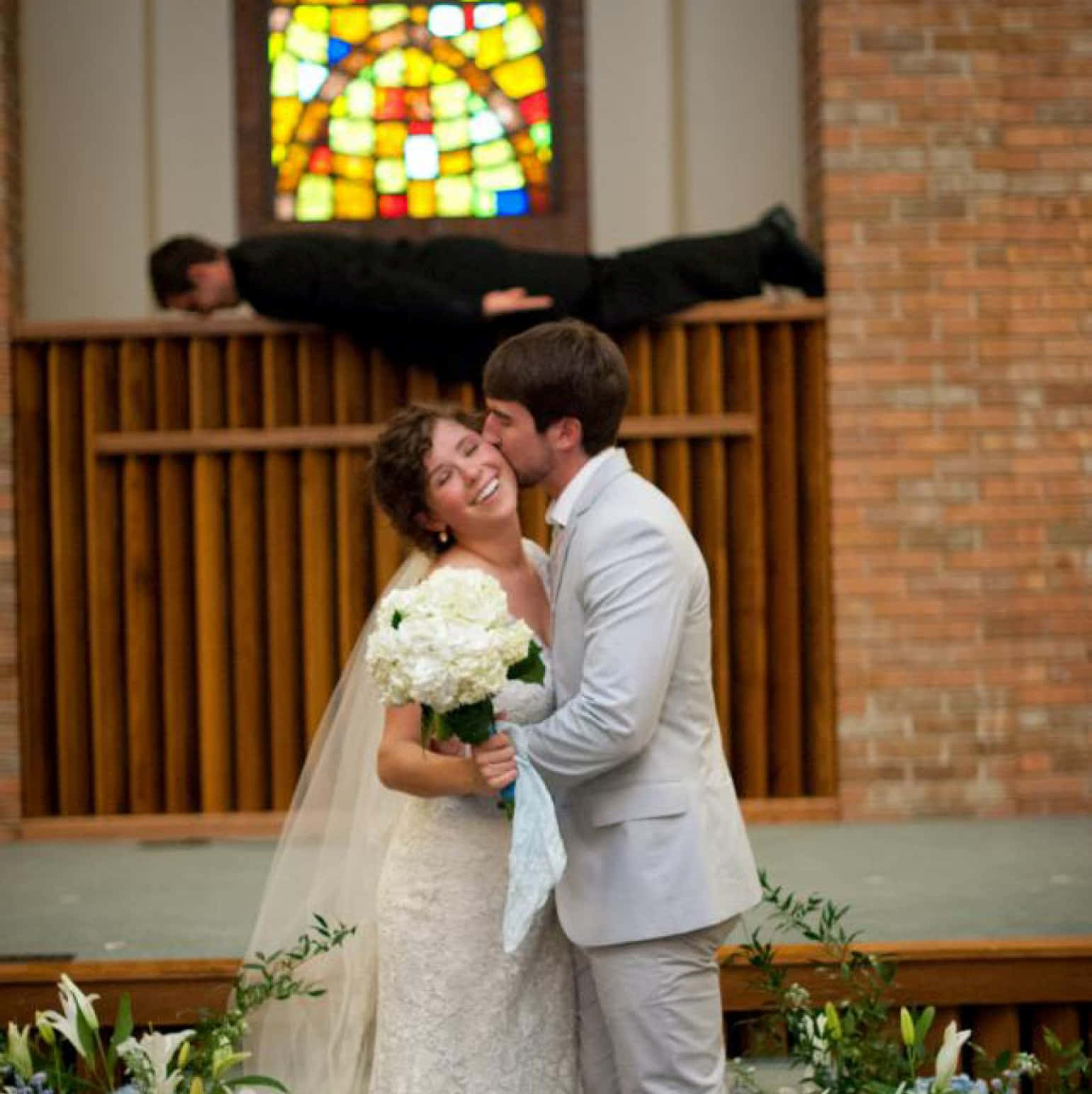 A Bride And Groom Kissing In Front Of A Stained Glass Window