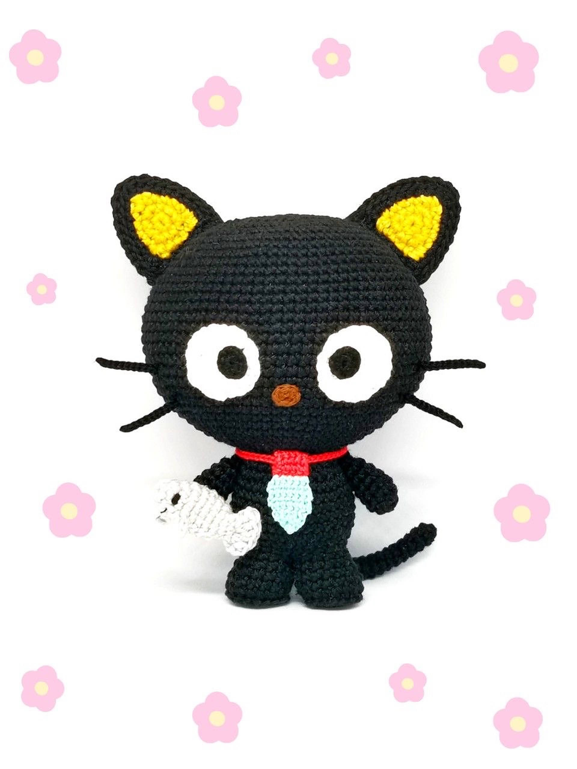 Stuffed Crochet Chococat Wallpaper — A handmade black crochet cat with yellow ears and red bow holds a white fish against a backdrop of pink flowers.