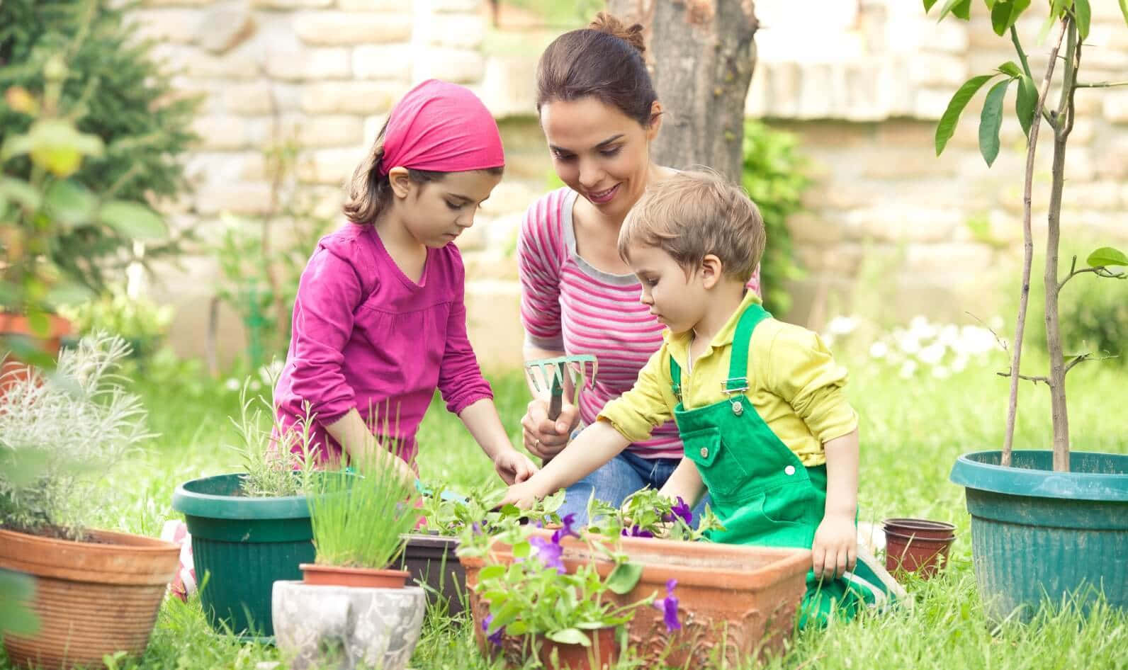 A Mother And Two Children Are Planting Flowers In The Garden