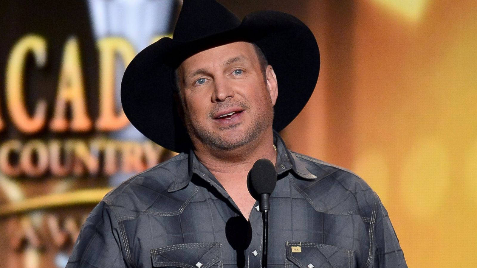 Bokeh Light Garth Brooks Wallpaper — A man in a black cowboy hat and plaid shirt speaks into a microphone at a country awards show with warm golden stage lighting.