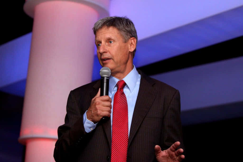 Gary Johnson With Microphone And Purple Backdrop Wallpaper