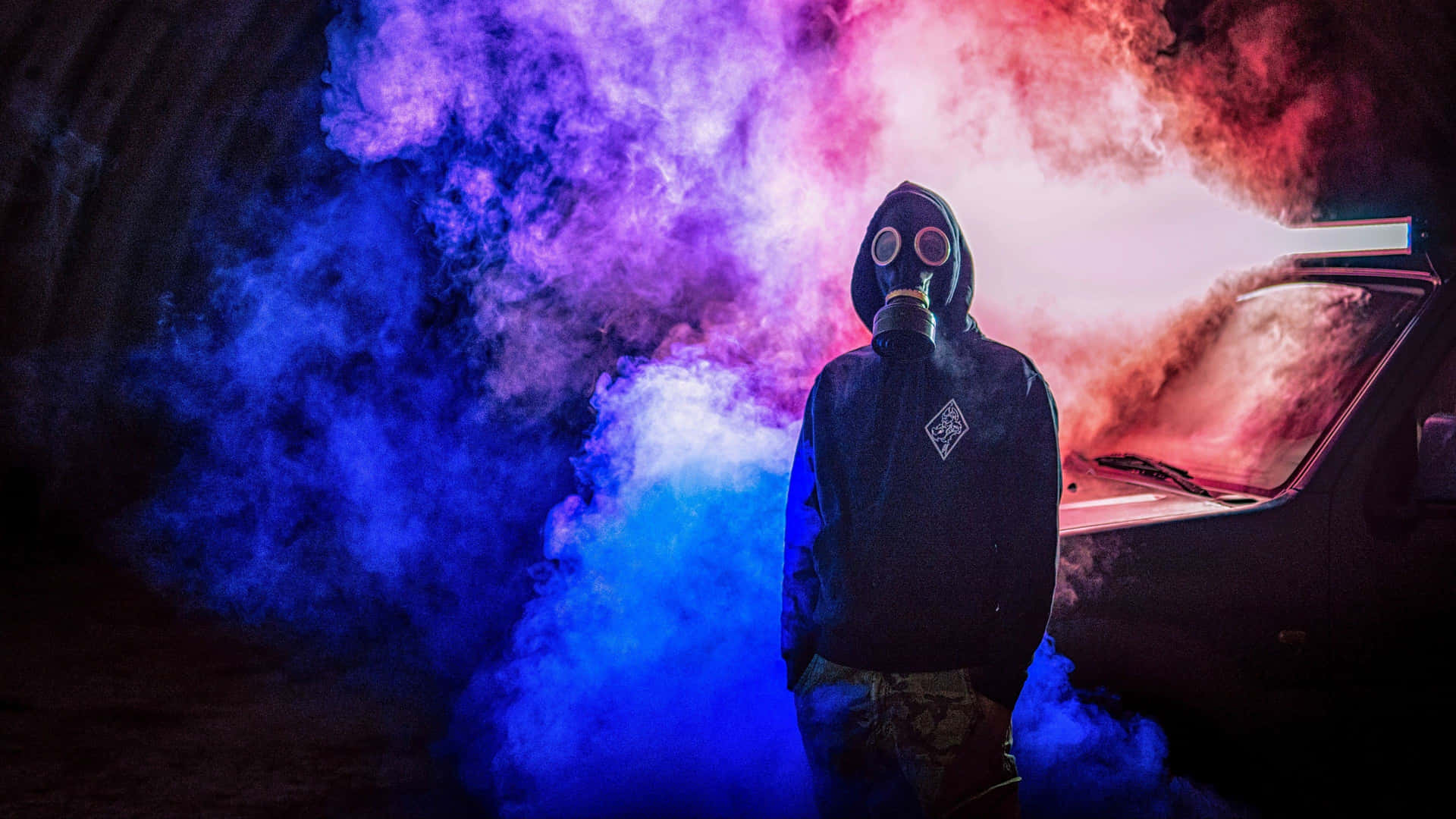 Gas Mask Figure Amidst Colorful Smoke Wallpaper