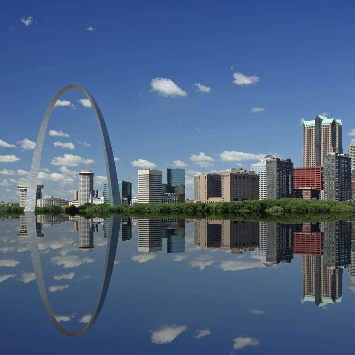 A Majestic View of the Gateway Arch and City Skyline Wallpaper — The Gateway Arch reflects perfectly in calm water beneath a bright blue sky with scattered clouds.