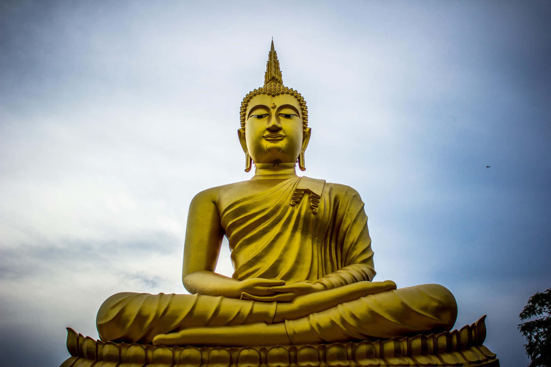 A Golden Buddha Statue Is Sitting In Front Of A Cloudy Sky