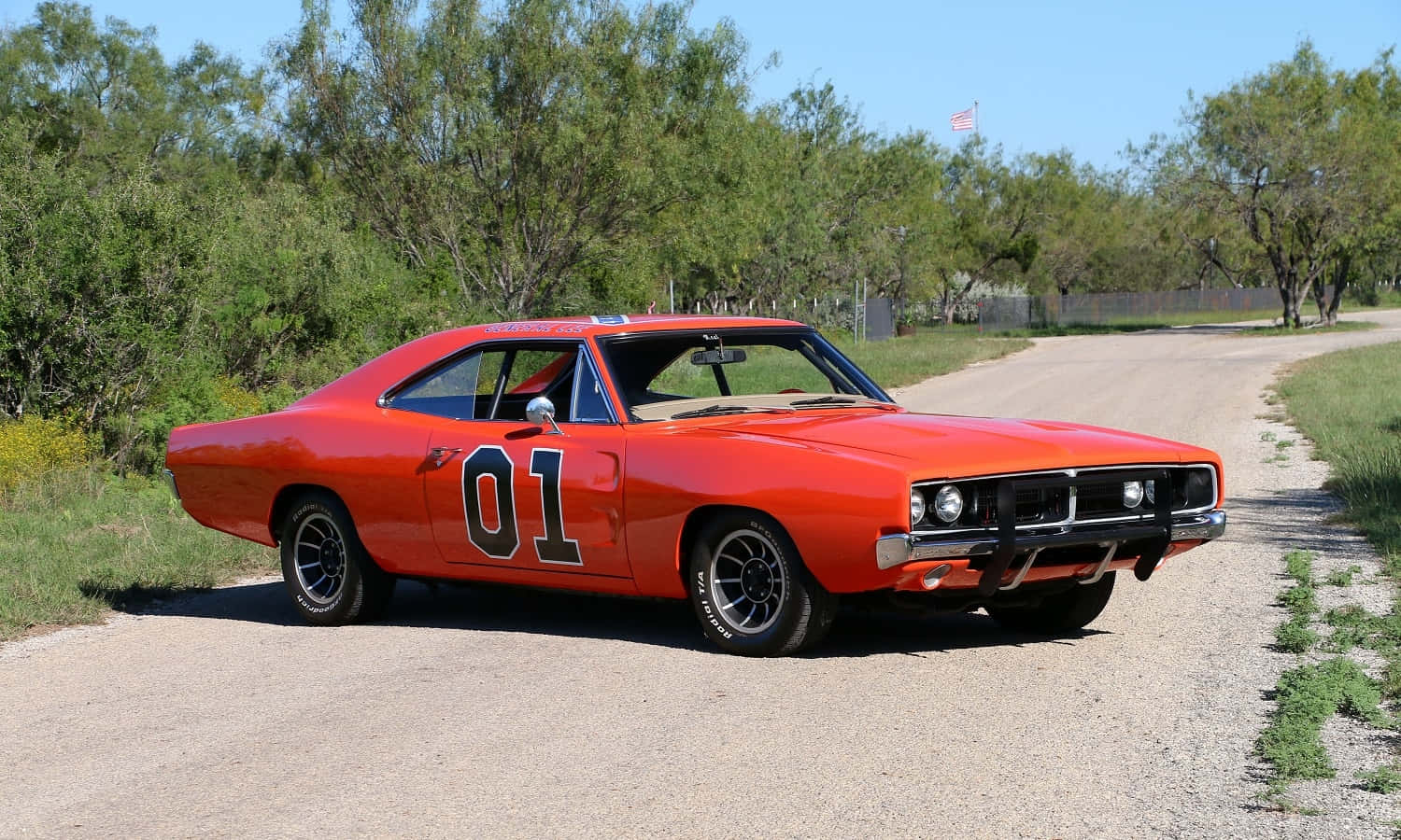 A Classic Orange Muscle Car Is Driving Down A Dirt Road Wallpaper