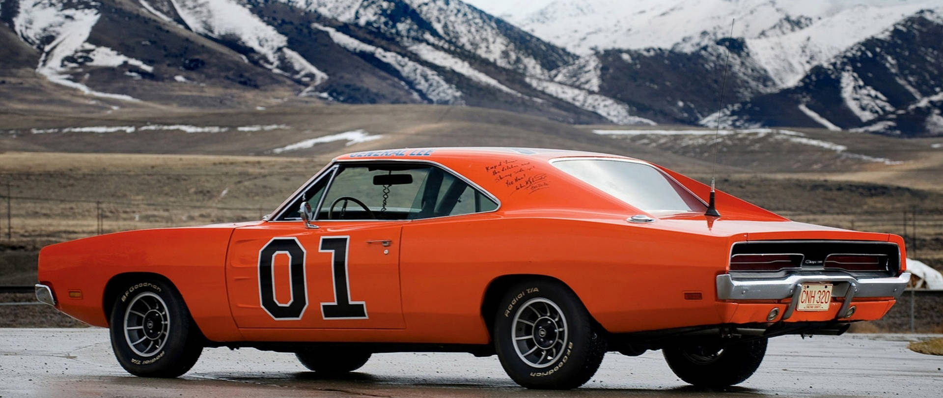 An Orange Dodge Charger Is Parked In Front Of Mountains Wallpaper