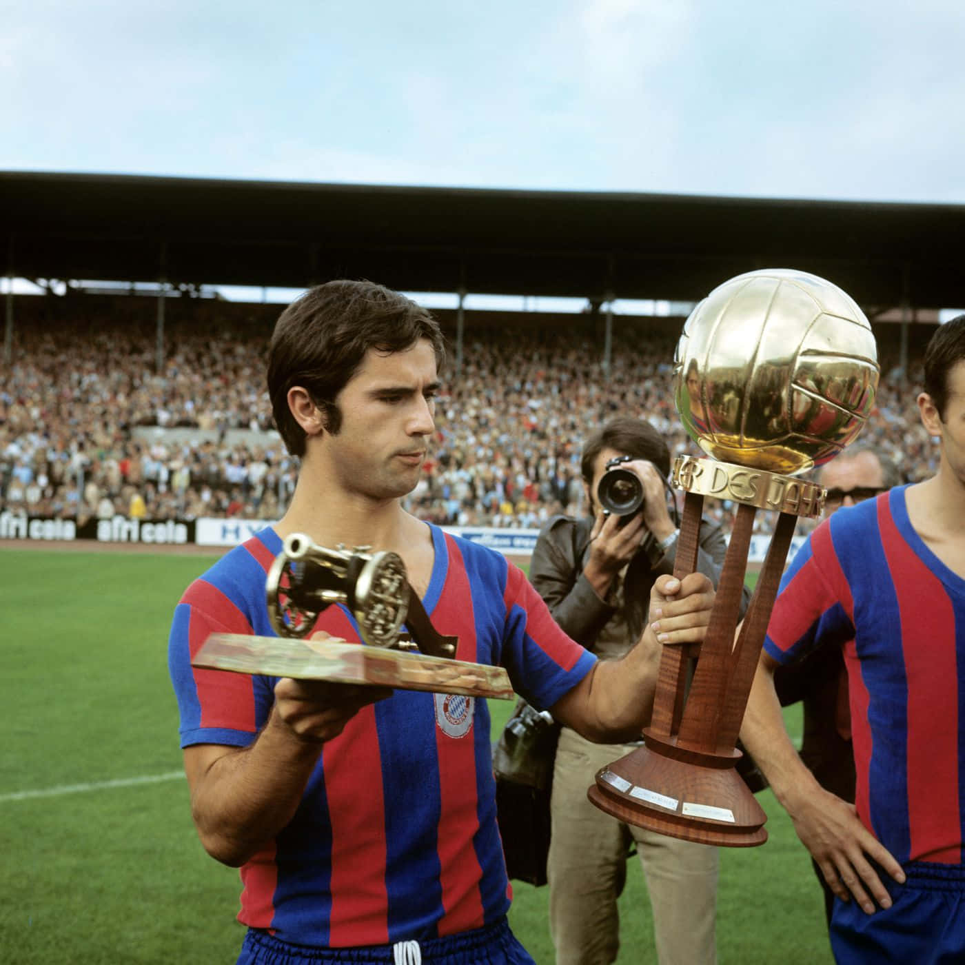 Legendary German Footballer Gerd Muller Triumphantly Holding Two Trophies Wallpaper