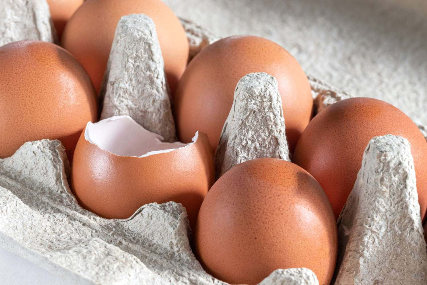 Get creative with Eggshell Wallpaper — Close-up of brown eggs in a cardboard tray with one cracked open revealing white interior.