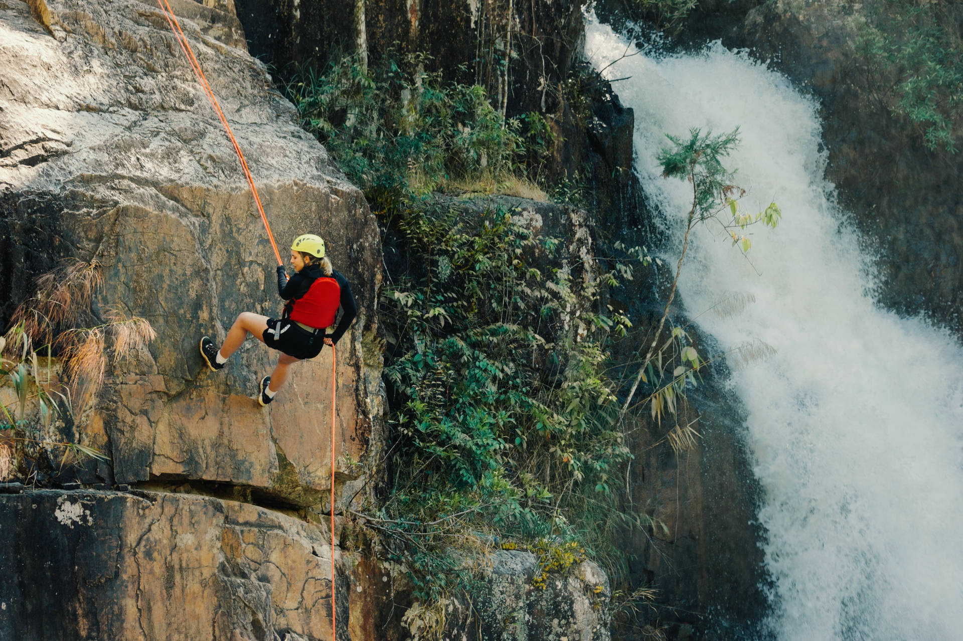 Girl Rock Climbing Near The Waterfalls Wallpaper