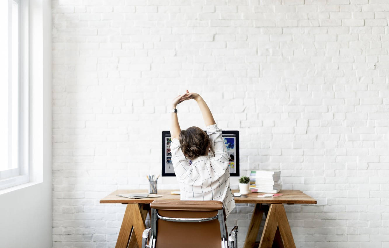 Young Professional Woman Stretching at Her Workplace Wallpaper