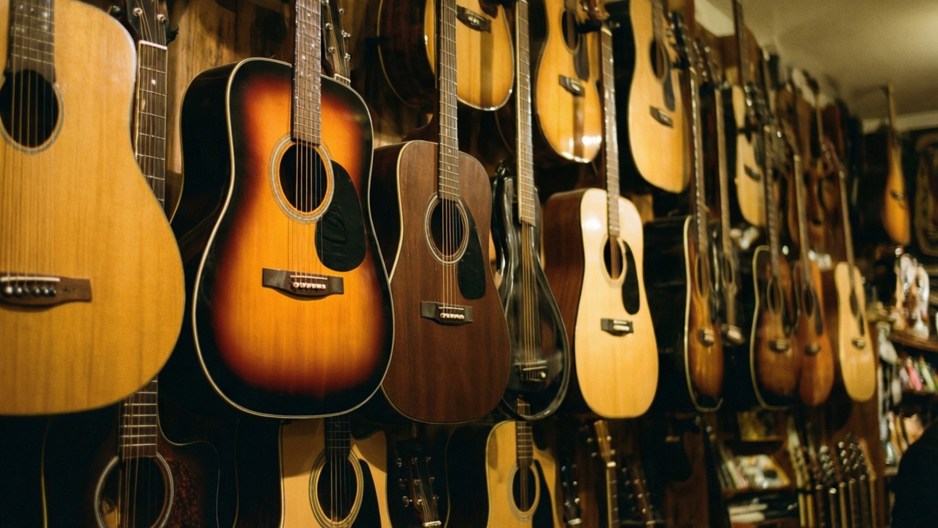 Guitar Gallery Wallpaper — Warmly lit acoustic guitars hang in a dense row on wooden walls in a cozy music shop.