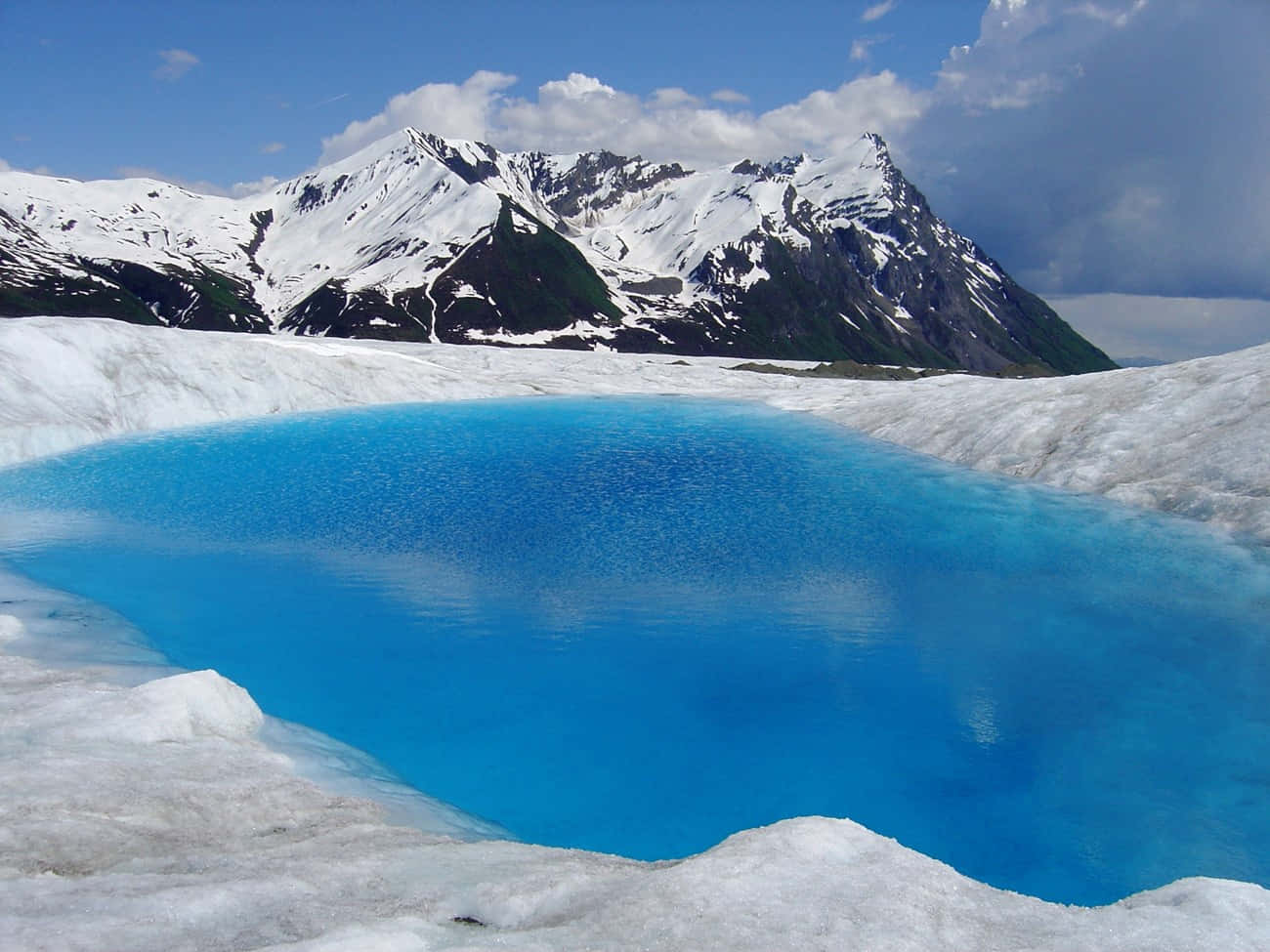 Glacial_ Blue_ Pond_ Amidst_ Snowy_ Mountains.jpg Wallpaper