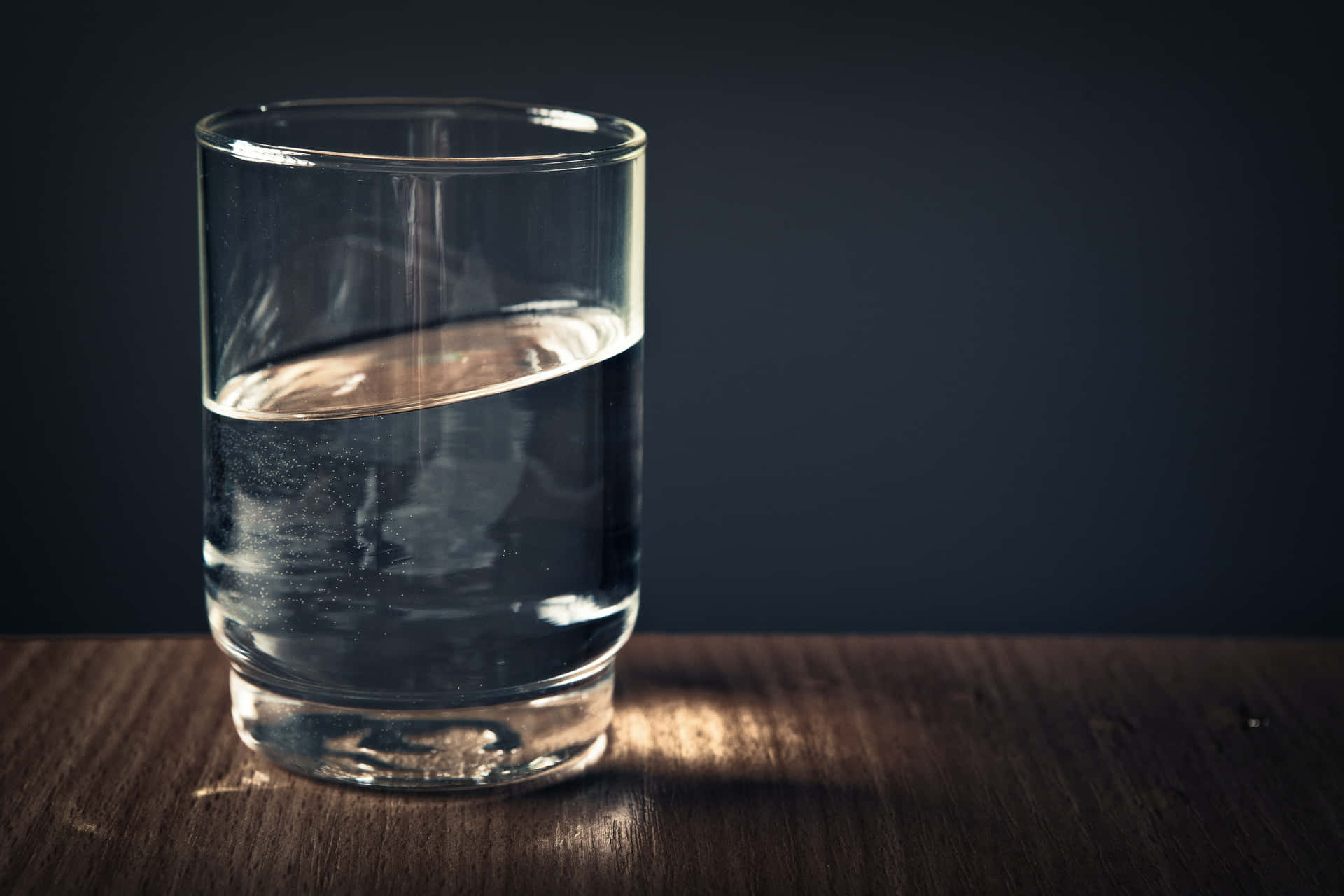 A Glass Of Water On A Table With Dark Background