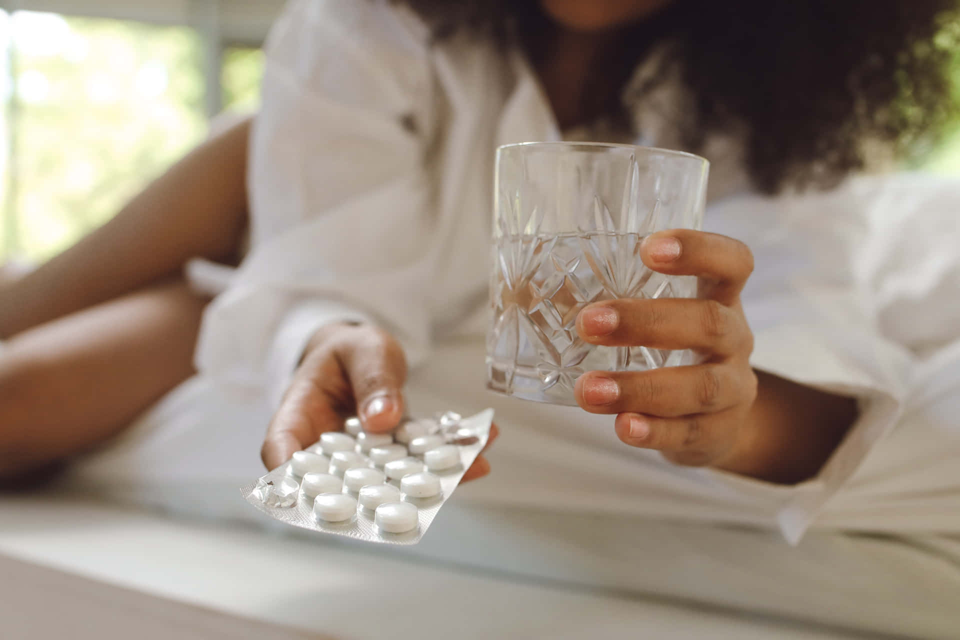 Woman Holding Pills And Water In Bed