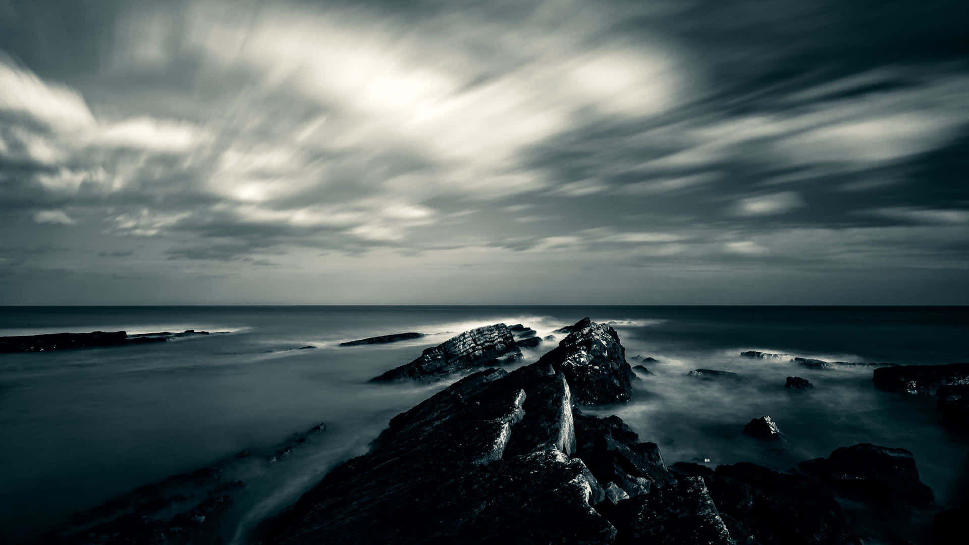 A Black And White Image Of A Rocky Shore With Clouds Wallpaper