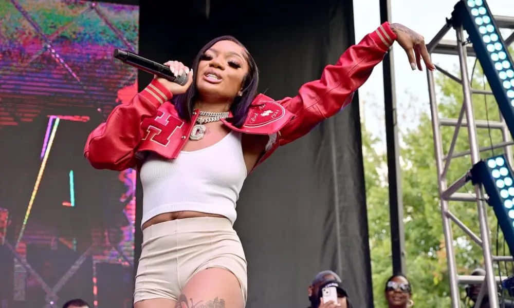A Woman In A Red Jacket And Shorts Singing On Stage Wallpaper