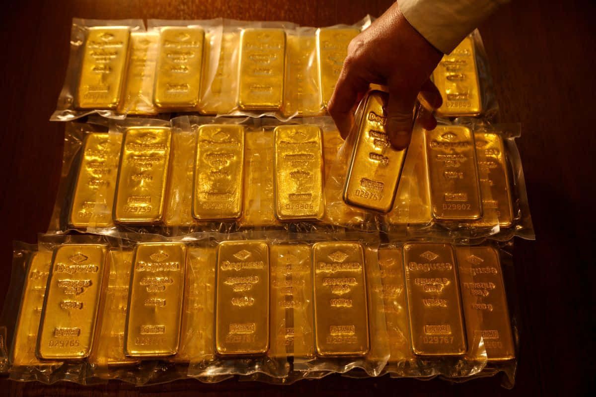 Download A Man Is Holding Gold Bars On A Table | Wallpapers.com