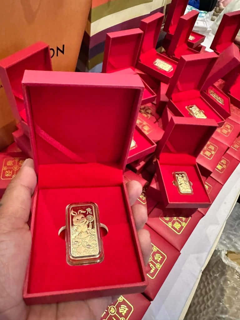 A Person Holding A Gold Bar In A Red Box