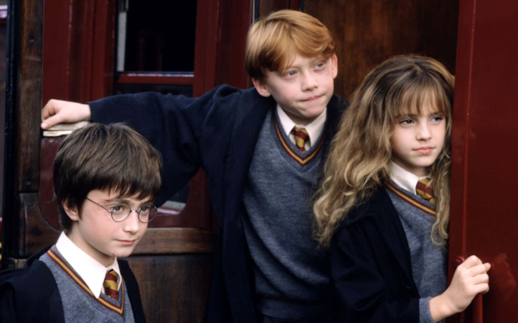 Harry Potter, Ron Weasley og Hermione Granger, Den Gyldne Trio, står højt mod et stærkt rødt strikket baggrund. Wallpaper