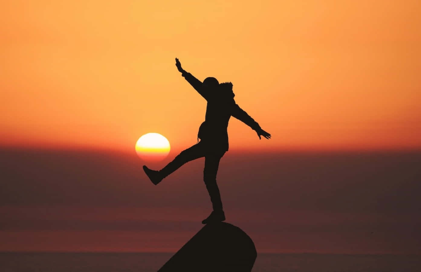 Silhouette Of A Woman Jumping On Top Of A Rock At Sunset