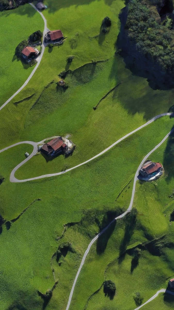 Et luftfoto af en grøn bakke med huse og en vej, der snor sig igennem den. Wallpaper