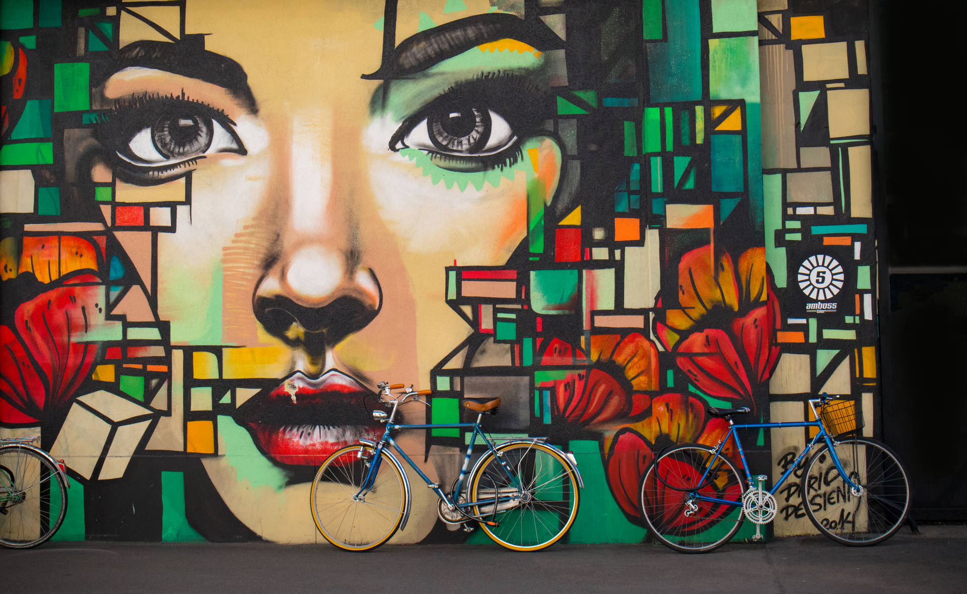Portrait graffiti of a beautiful woman with colorful shapes on the side and bicycles leaning on the wall.
