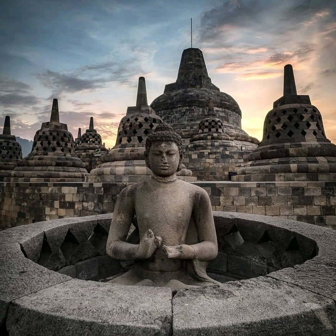 Harmonious Serenity: A statue of Buddha overlooking the magnificent Borobudur Temple Wallpaper