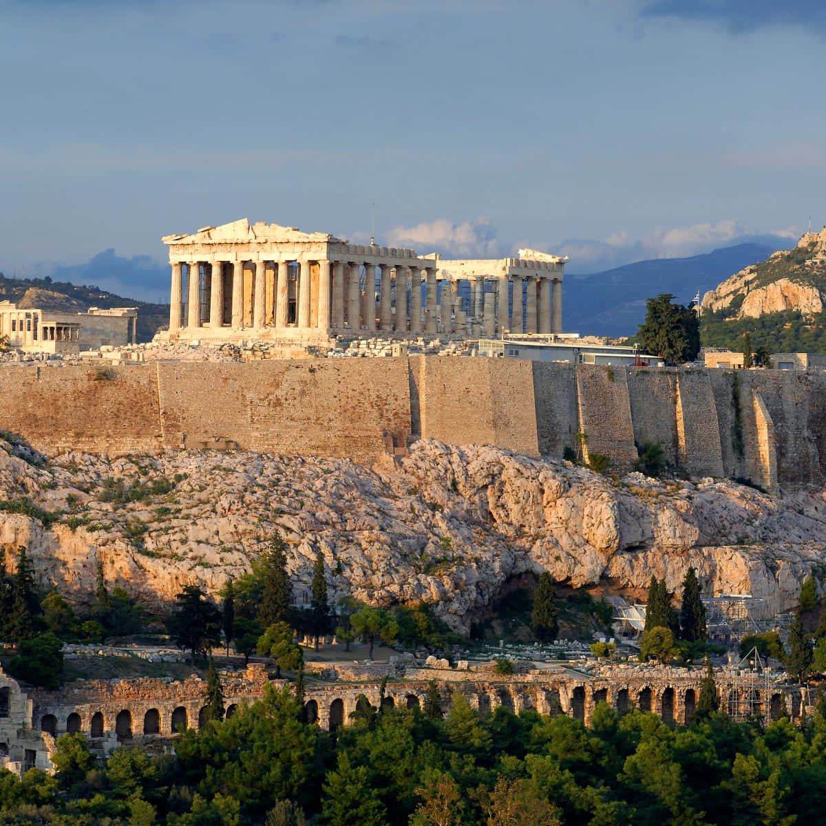 The Parthenon Is Atop A Hill With Trees And A View Of The City