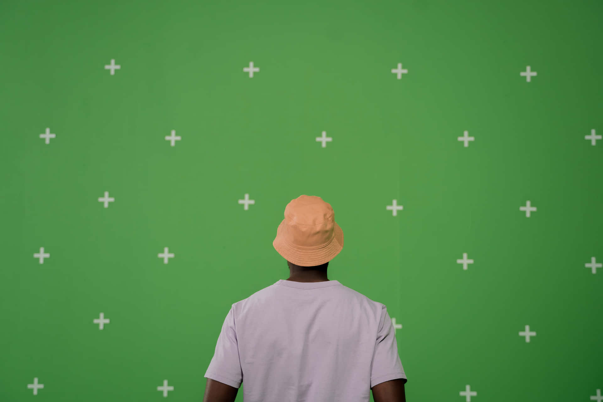 A Man In A Hat Standing In Front Of A Green Wall
