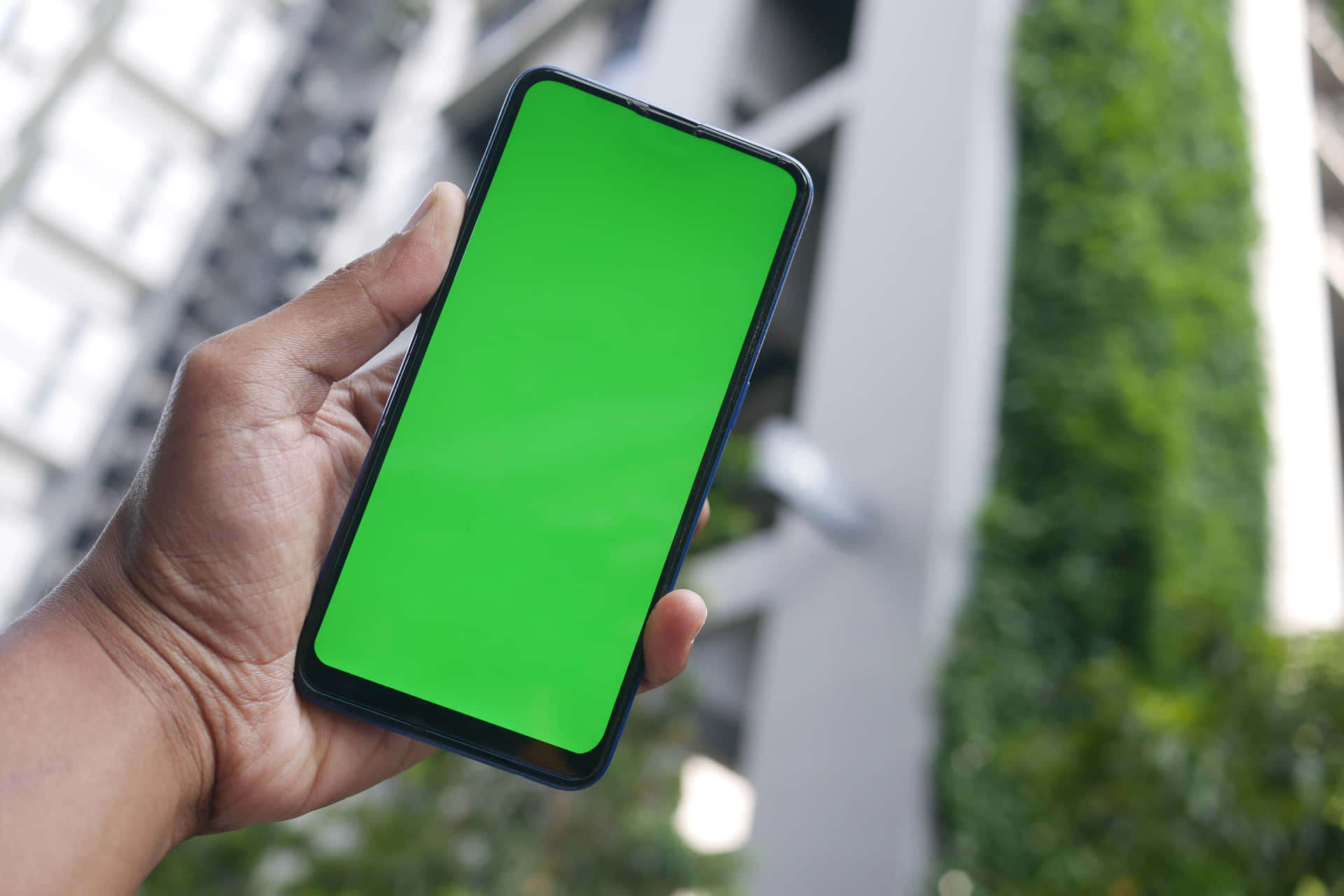 Enmand Holder En Smartphone Med En Grøn Skærm Foran En Bygning.