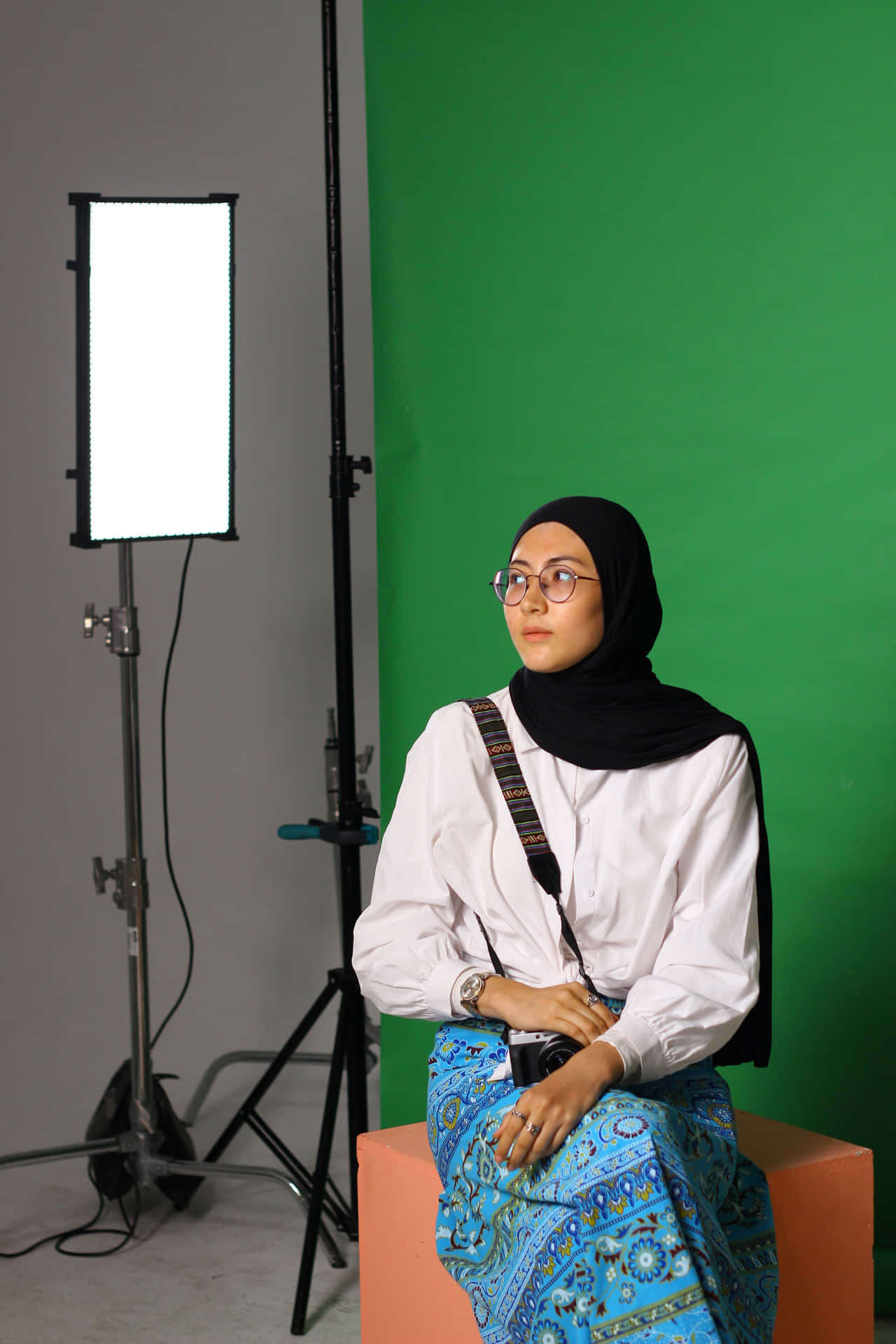 A Woman In A Hijab Sitting On A Stool In Front Of A Green Screen