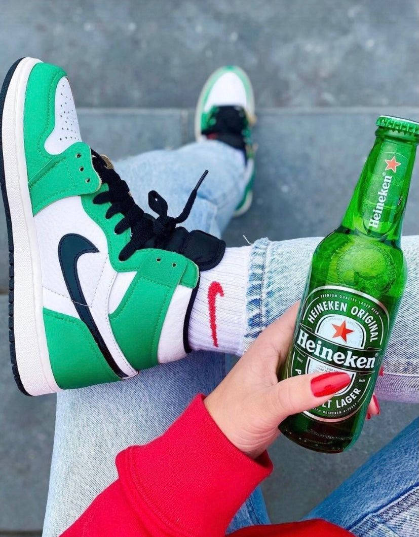 En person holder en Heineken øl og et par grønne sneakers. Wallpaper