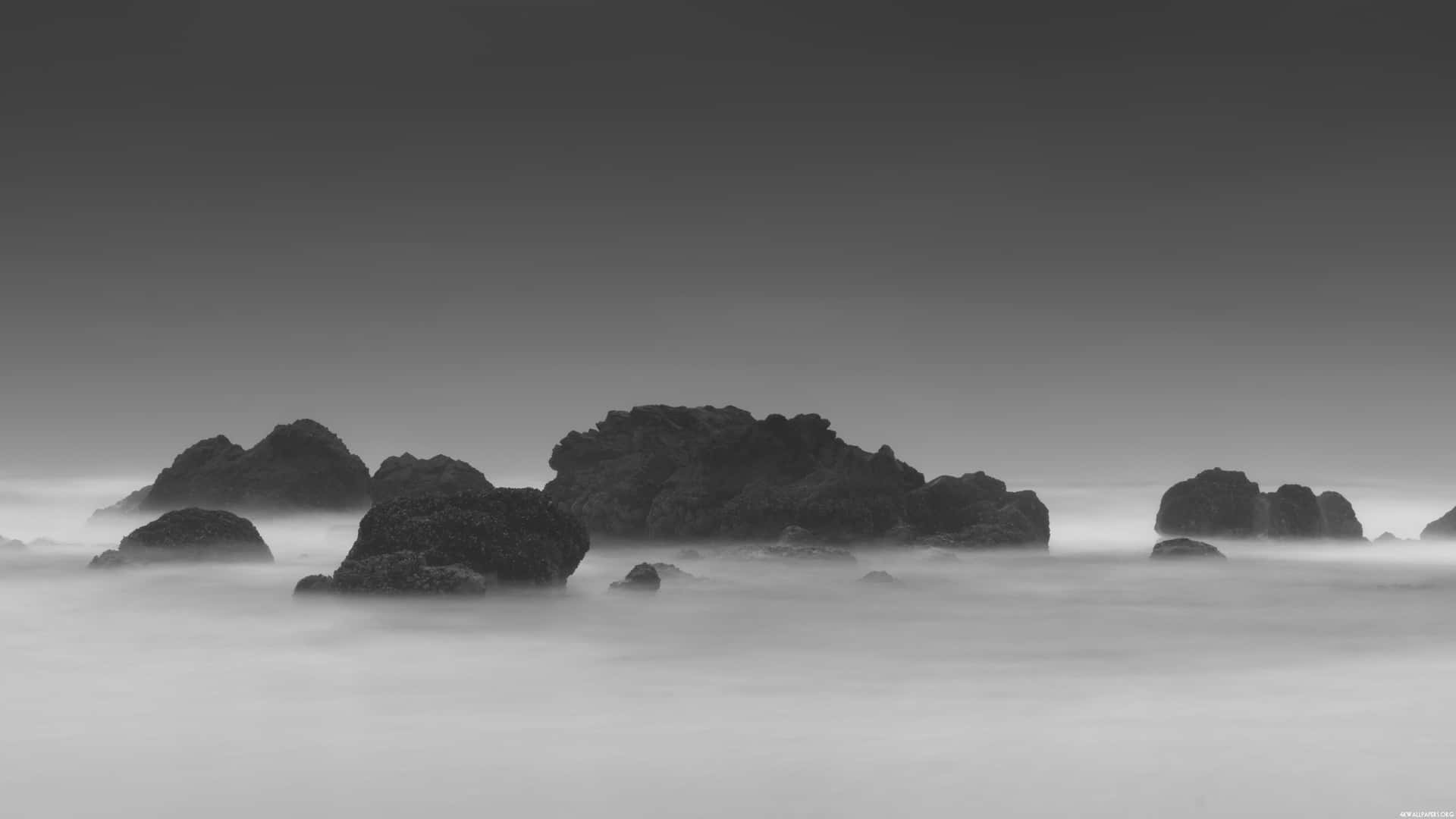 A Black And White Photo Of Rocks In The Ocean Wallpaper