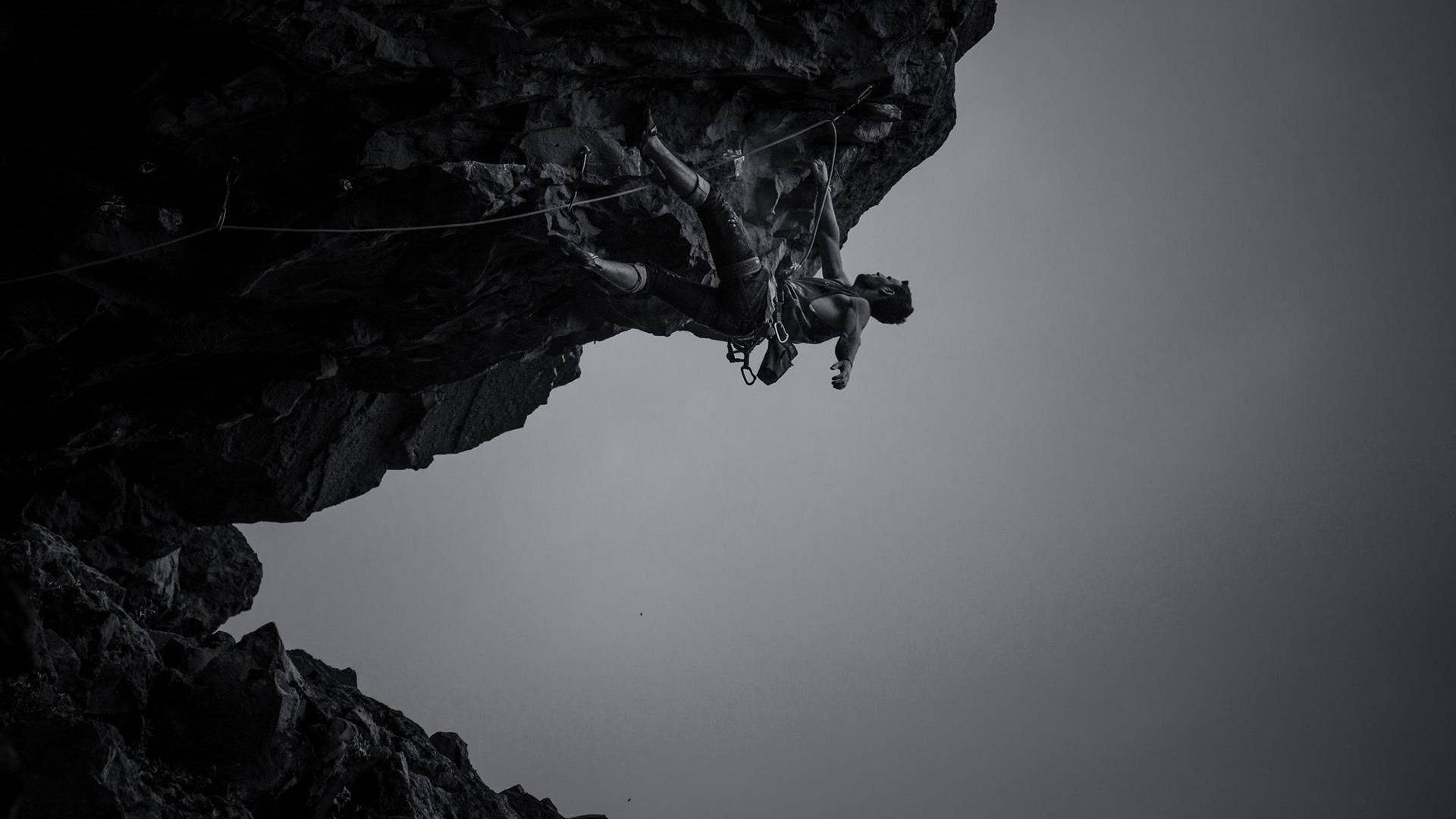 Sort-hvid foto af mand, der klatrer på klipper Wallpaper