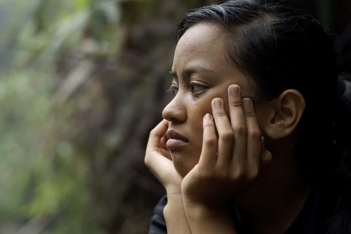 A Woman Is Sitting In The Forest With Her Hand On Her Face