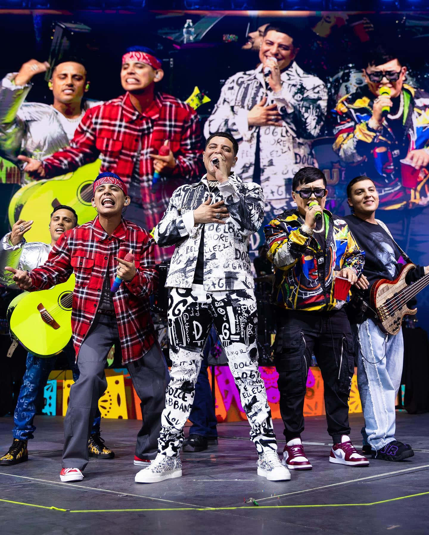 A Group Of Men Standing On Stage With A Colorful Background Wallpaper